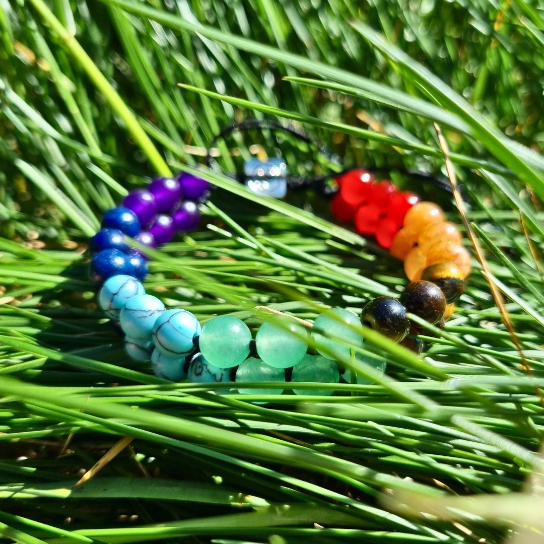 Handmade bracelet with 7 chakra crystal gemstones, featuring amethyst, lapis lazuli, blue aquamarine, green aventurine, tiger’s eye, orange stone, and red agate. The bracelet is between the grass.