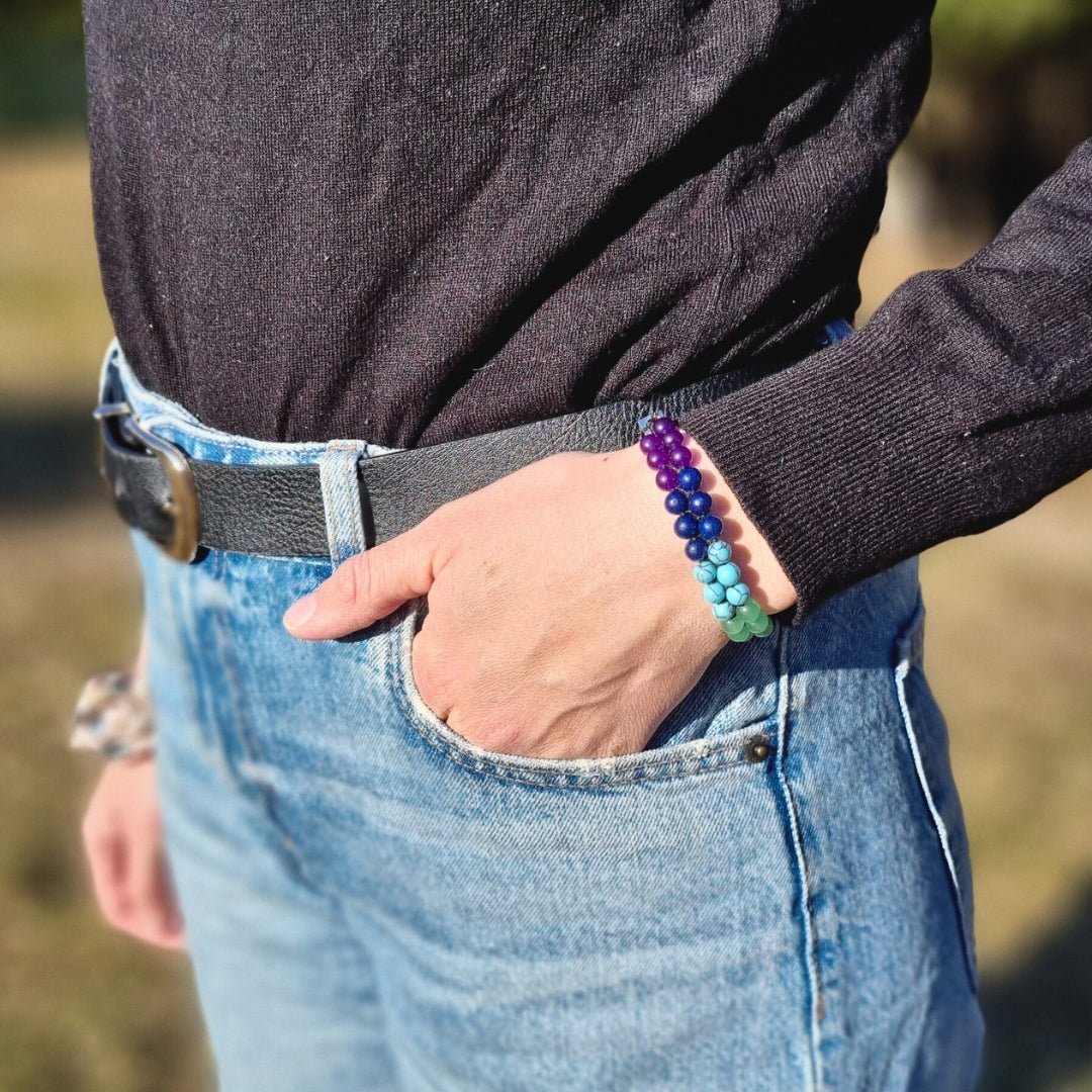 A woman wearing a handmade bracelet with 7 chakra crystal gemstones, featuring amethyst, lapis lazuli, blue aquamarine, green aventurine, tiger’s eye, orange stone, and red agate. Her hand is in the pocket, looking like a lifestyle photo.