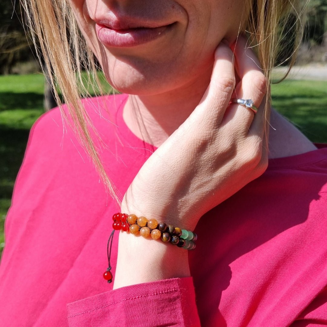 A woman wearing a handmade bracelet with 7 chakra crystal gemstones, featuring amethyst, lapis lazuli, blue aquamarine, green aventurine, tiger’s eye, orange stone, and red agate."