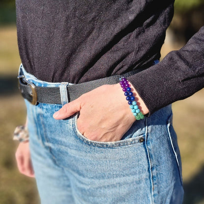 A woman wearing a handmade bracelet with 7 chakra crystal gemstones, featuring amethyst, lapis lazuli, blue aquamarine, green aventurine, tiger’s eye, orange stone, and red agate. Her hand is in the pocket, looking like a lifestyle photo.