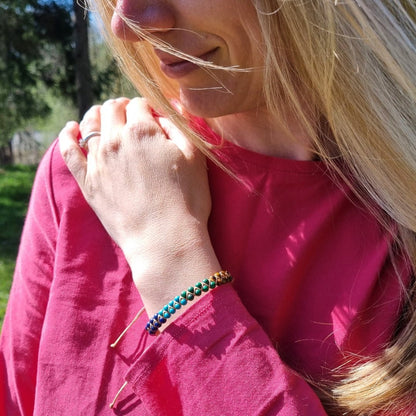 A woman wearing a handmade bracelet with 7 chakra crystal gemstones, featuring amethyst, lapis lazuli, turquoise,  malachite, tiger’s eye, sunstone, and red agate.