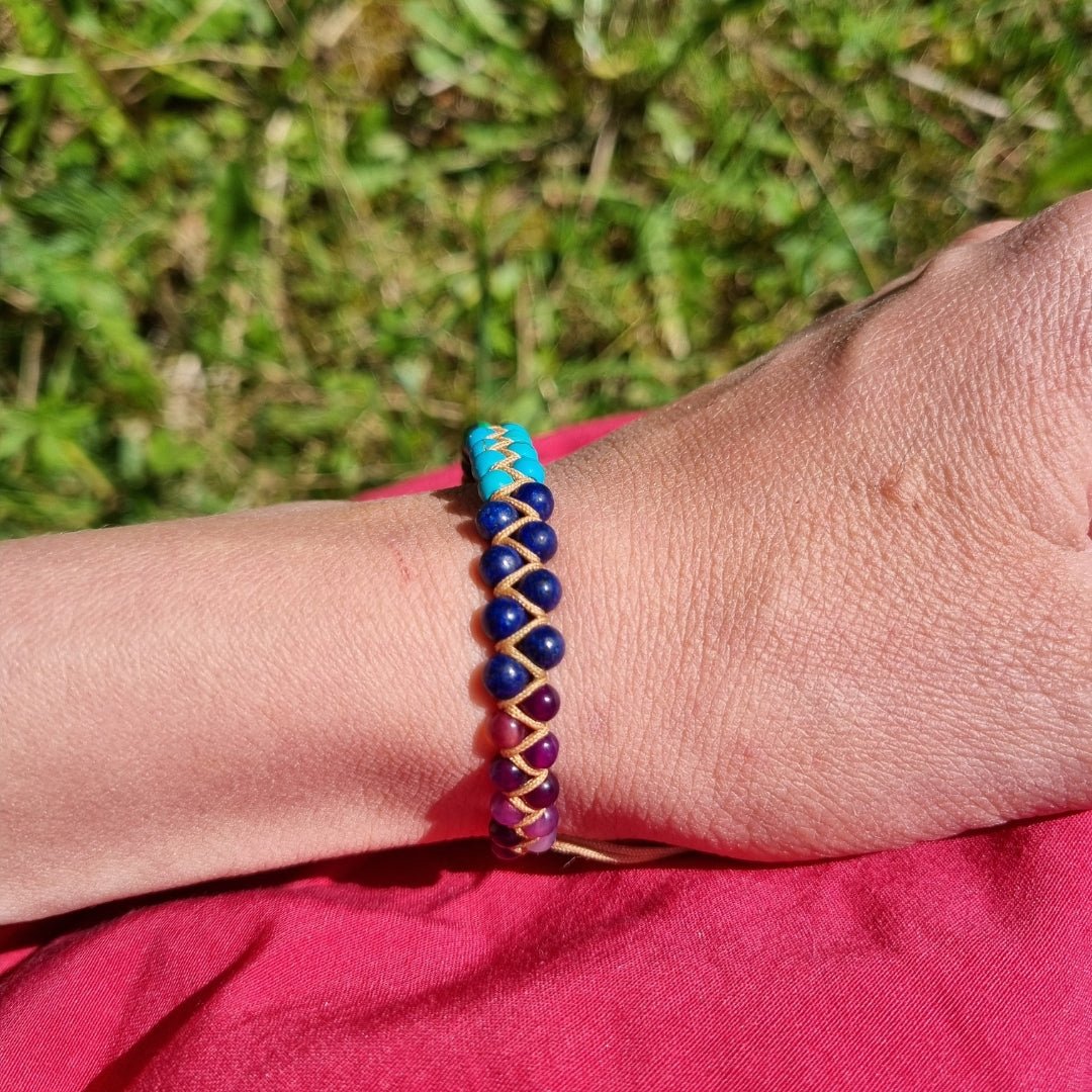 A hand wearing a handmade bracelet with 7 chakra crystal gemstones, featuring amethyst, lapis lazuli, turquoise,  malachite, tiger’s eye, sunstone, and red agate. 