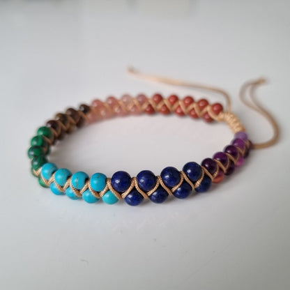 Handmade bracelet with 7 chakra crystal gemstones, featuring amethyst, lapis lazuli, turquoise,  malachite, tiger’s eye, sunstone, and red agate. The bracelet is positioned on a white surface. 
